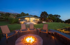 Huge backyard at dusk featuring chairs around a lit fire pit. 