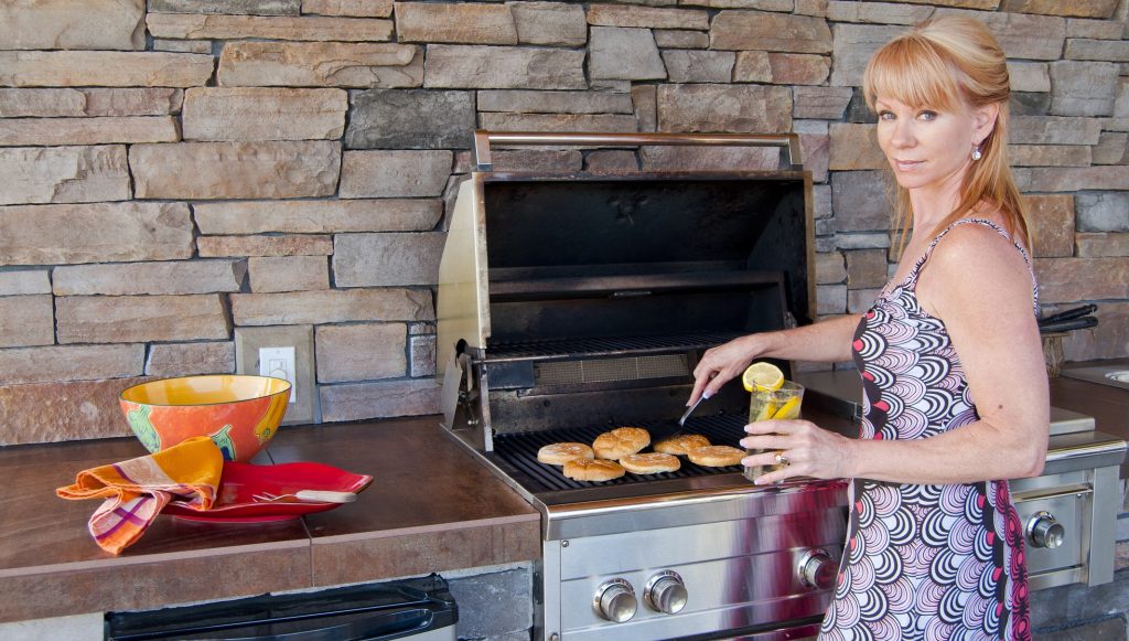 blonde woman cooking some delicious food in her outdoor kitchen