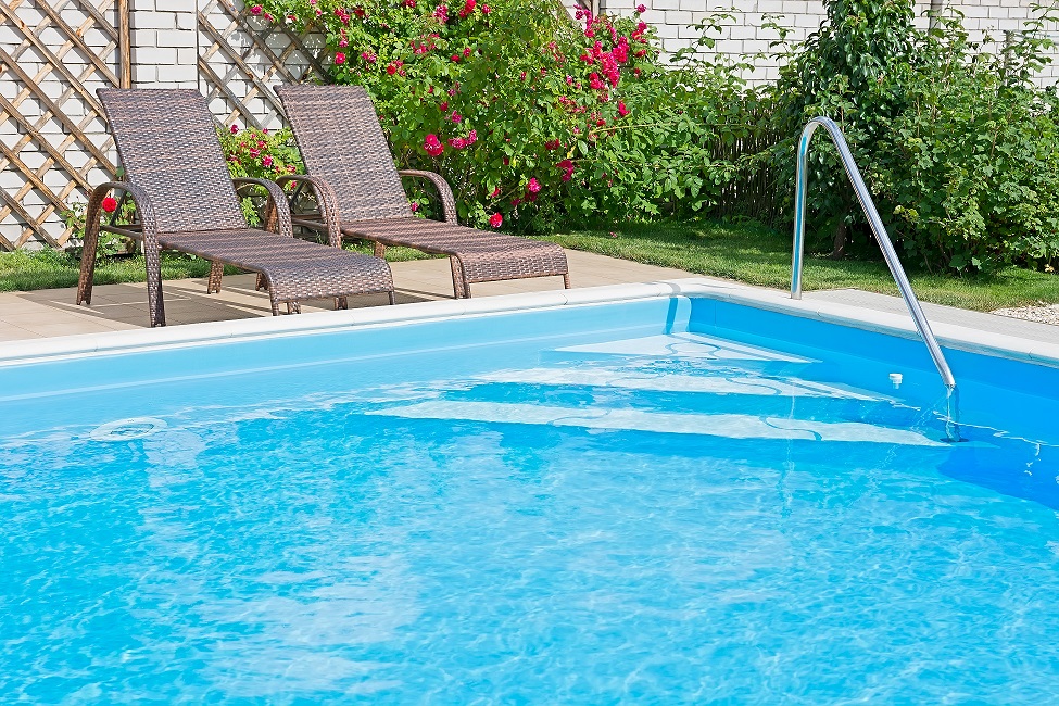 Swimming pool with blue water on a sunny day. Recreation area with a fragment of garden and outdoor furniture.