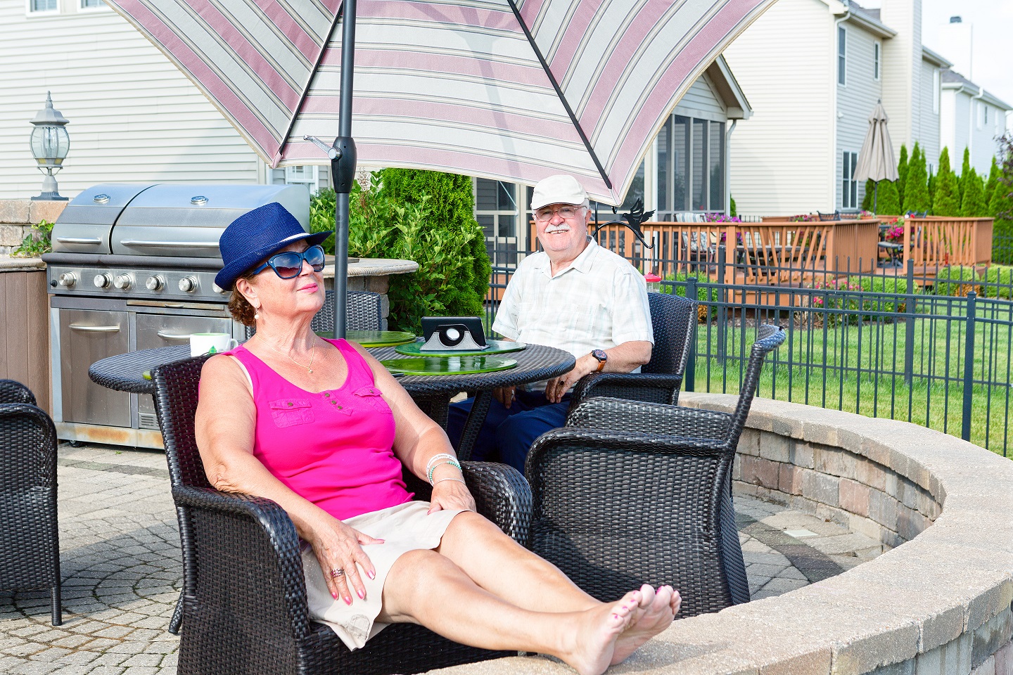 Elderly couple relaxing on an upmarket paved circular patio in the hot summer sun chilling out and enjoying the vacation in a comfortable armchair