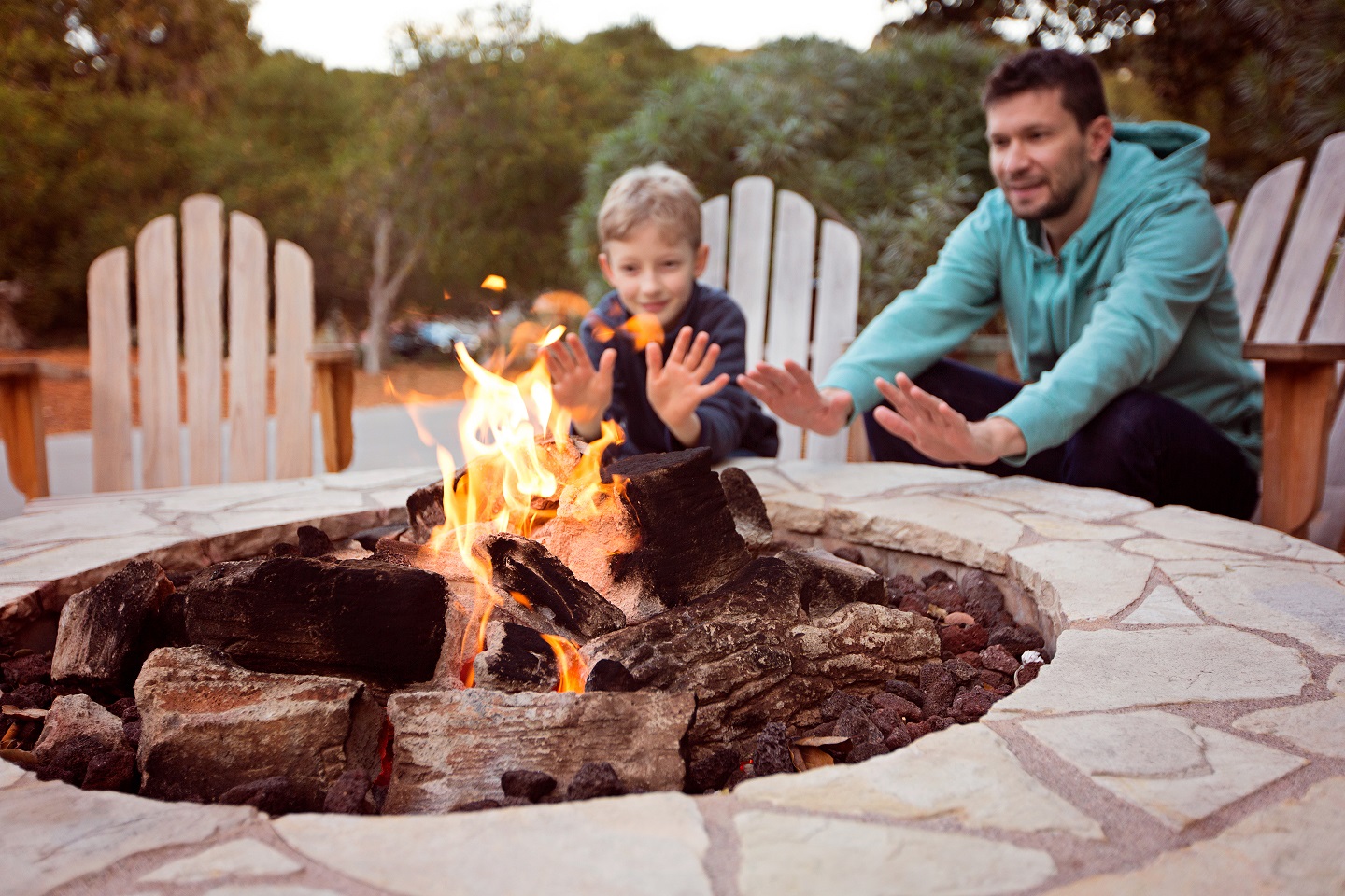 open outdoor fireplace with man and little boy warming their hands, sitting behind it. 